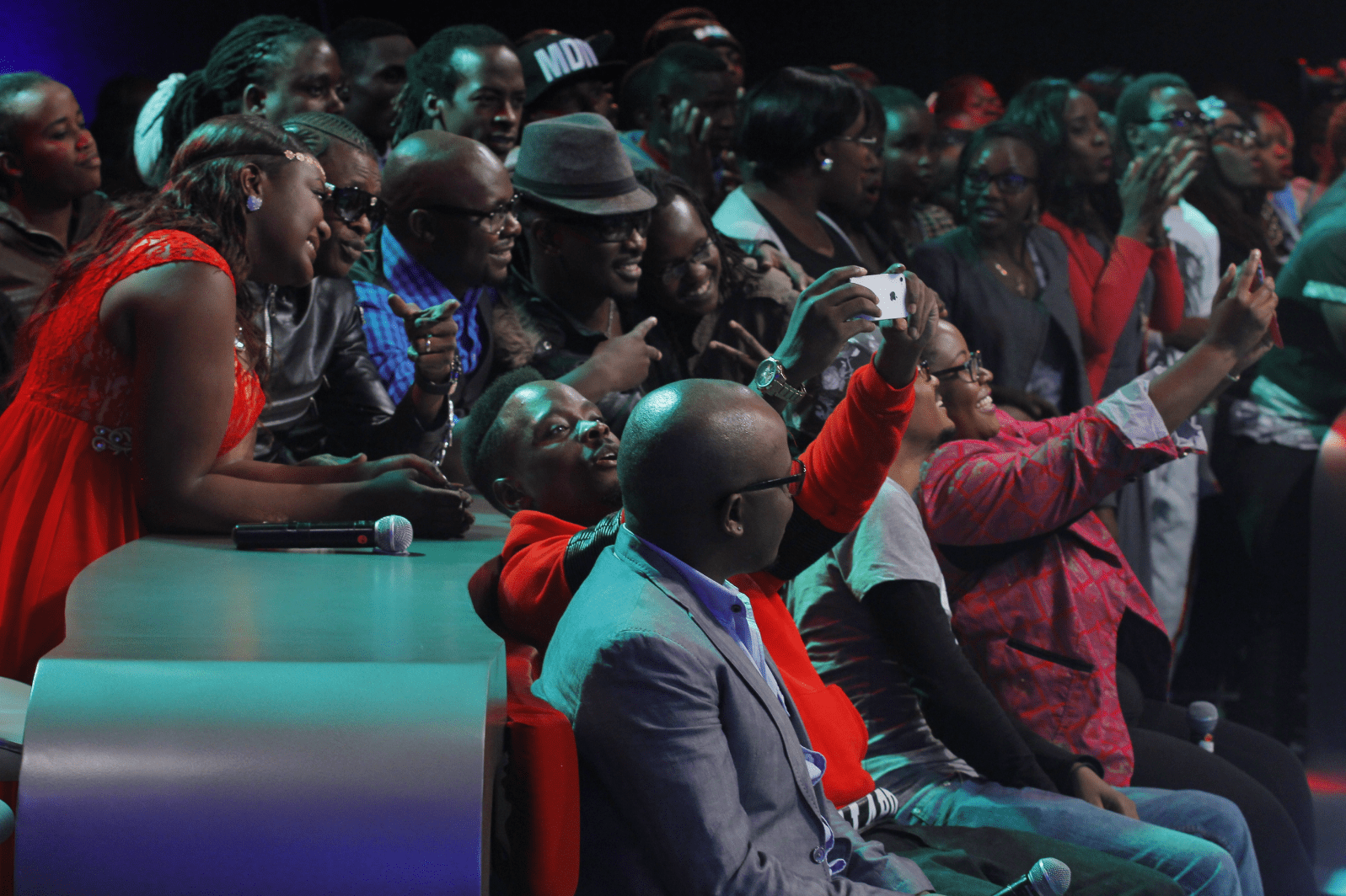 Side view of a studio audience clapping and recording a show on their phones